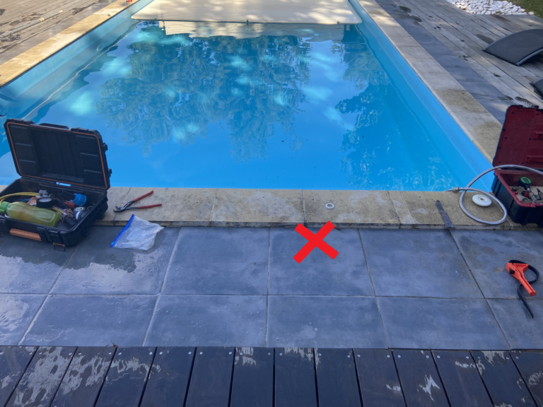 Croix rouge au sol localisant une fuite sur canalisation de piscine sous terrasse carrelée à Andernos-les-Bains